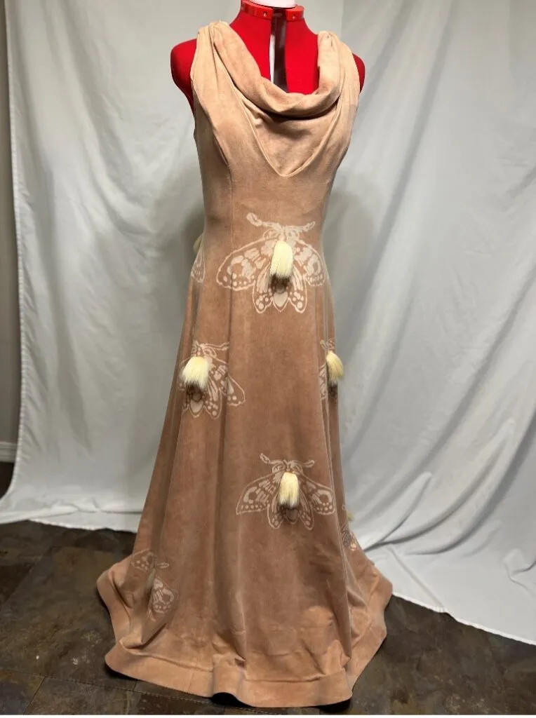 A long, tan dress displayed on a dress form, featuring printed moth designs accented with small cream-colored tassels.